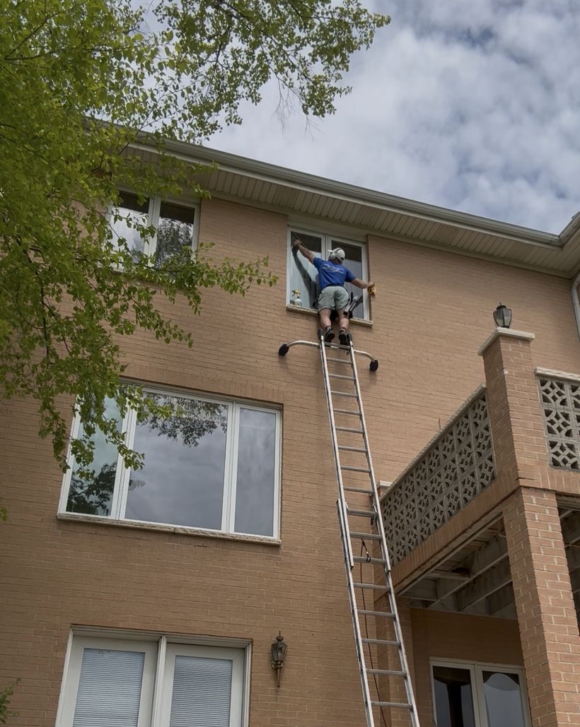 Davey cleaning a third-story window from an extension ladder